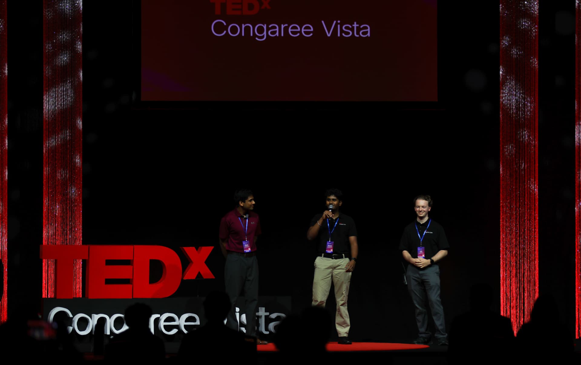 Three TEDxCongaree Vista organizers standing on stage in front of the event's title screen